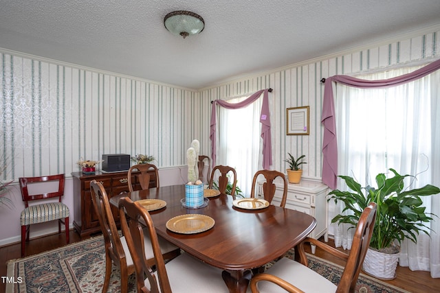 dining space with a textured ceiling, wallpapered walls, and wood finished floors
