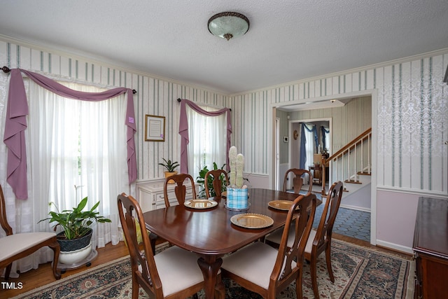 dining space with crown molding, stairs, wood finished floors, wallpapered walls, and a textured ceiling