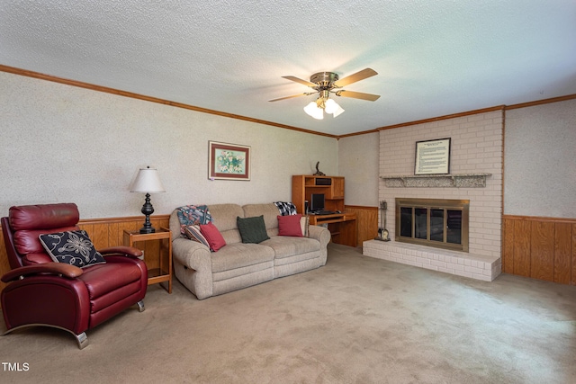 living room with ceiling fan, wainscoting, a brick fireplace, wooden walls, and ornamental molding