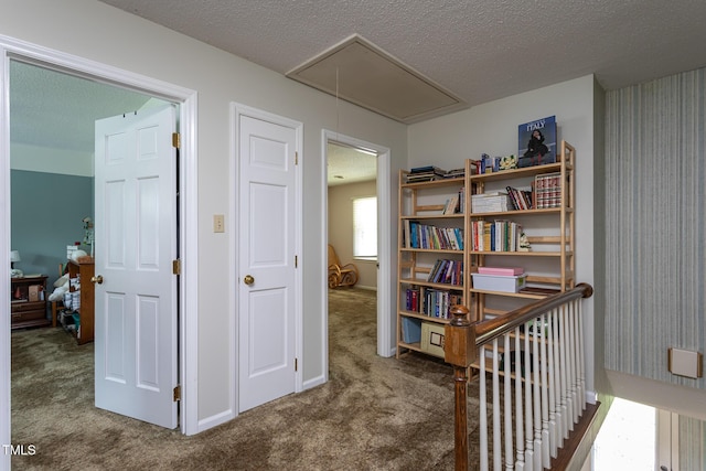 hallway with attic access, carpet flooring, and a textured ceiling