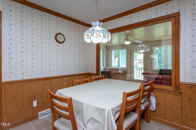 tiled dining area with wooden walls, ornamental molding, wainscoting, and visible vents