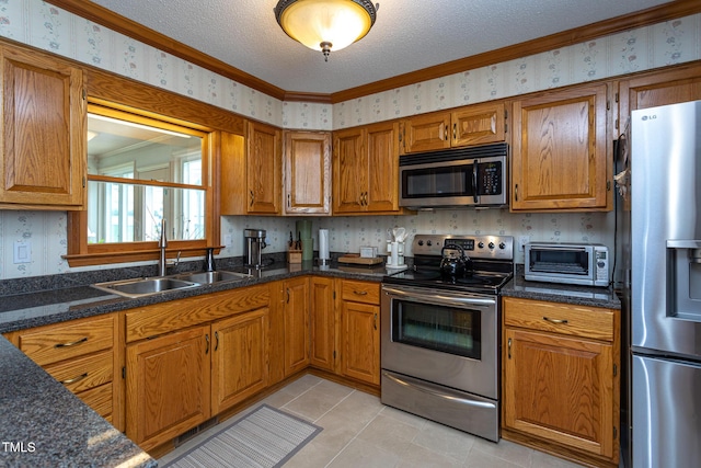 kitchen with brown cabinetry, appliances with stainless steel finishes, a sink, a toaster, and wallpapered walls
