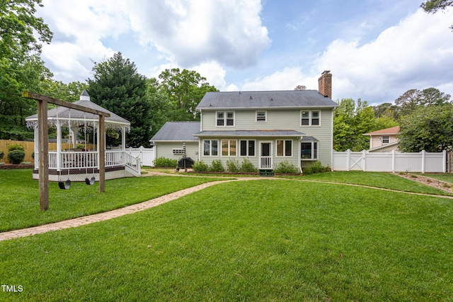 back of property with a wooden deck, a fenced backyard, a chimney, a gazebo, and a yard