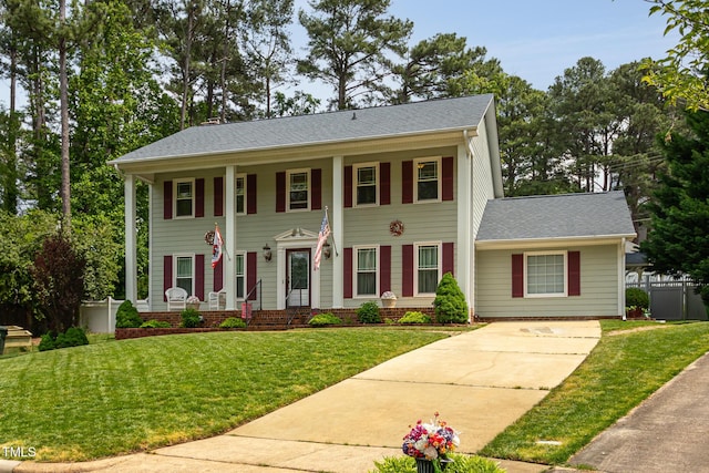 greek revival inspired property with covered porch, concrete driveway, and a front lawn