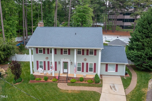 view of front of house with covered porch, a chimney, a front yard, fence, and a shingled roof