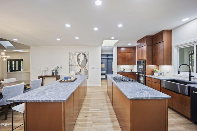 kitchen featuring a large island, a skylight, modern cabinets, a sink, and light wood-style flooring