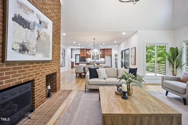 living area featuring a brick fireplace, a towering ceiling, light wood-type flooring, recessed lighting, and a notable chandelier