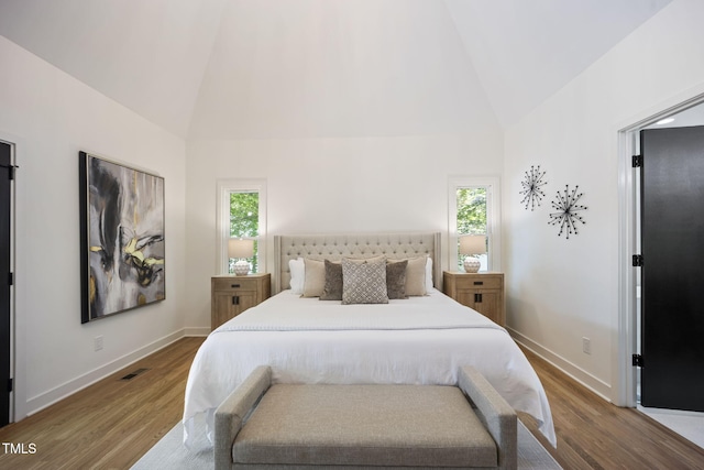 bedroom featuring baseboards, wood finished floors, visible vents, and high vaulted ceiling