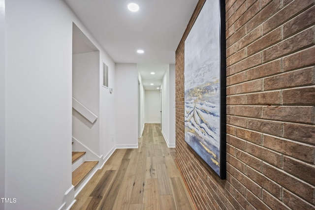 hallway with brick wall, wood finished floors, baseboards, an accent wall, and recessed lighting