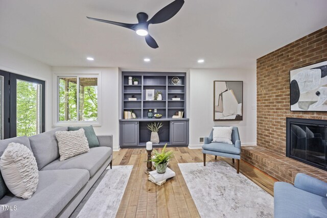 living room featuring a brick fireplace, a ceiling fan, recessed lighting, light wood-type flooring, and visible vents