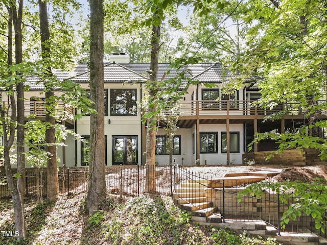 back of house with stucco siding, a chimney, fence private yard, and a balcony