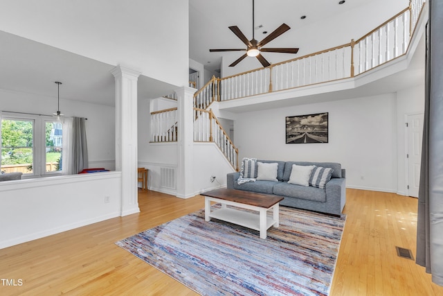 living room featuring a ceiling fan, visible vents, wood finished floors, and a towering ceiling