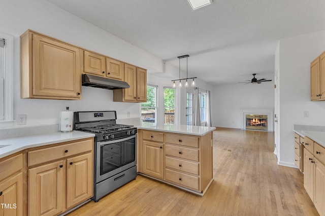 kitchen featuring stainless steel range with gas stovetop, a peninsula, light brown cabinetry, and under cabinet range hood