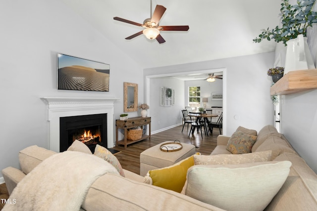 living room with wood finished floors, baseboards, a warm lit fireplace, high vaulted ceiling, and a ceiling fan