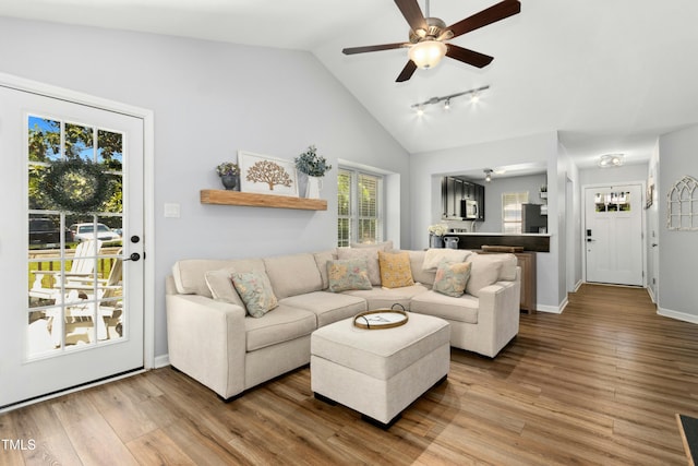 living area with track lighting, a ceiling fan, vaulted ceiling, and wood finished floors