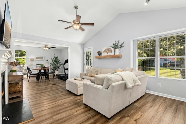 living room featuring wood finished floors, a fireplace, baseboards, high vaulted ceiling, and a ceiling fan