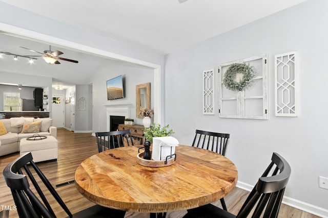 dining space featuring lofted ceiling, a fireplace, baseboards, a ceiling fan, and light wood finished floors