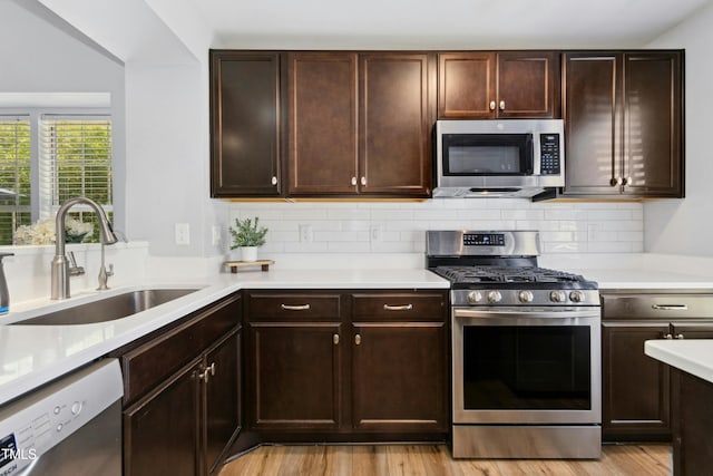 kitchen featuring appliances with stainless steel finishes, a sink, light countertops, light wood-style flooring, and tasteful backsplash