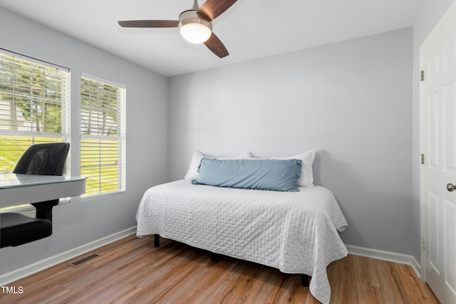 bedroom featuring baseboards, visible vents, multiple windows, and wood finished floors