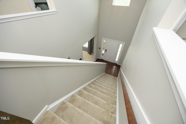 stairs featuring baseboards, a towering ceiling, and carpet floors
