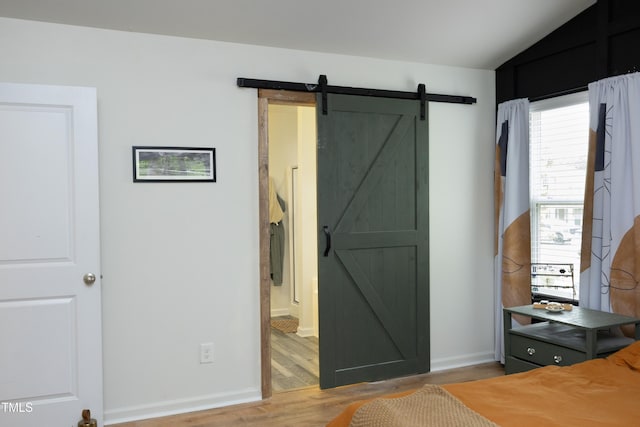 bedroom featuring baseboards, vaulted ceiling, a barn door, and light wood-style flooring