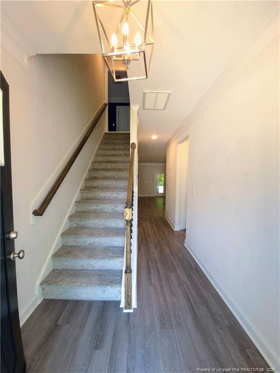 stairway with an inviting chandelier, baseboards, ornamental molding, and wood finished floors