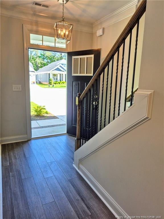 foyer entrance with visible vents, crown molding, wood finished floors, stairway, and a chandelier