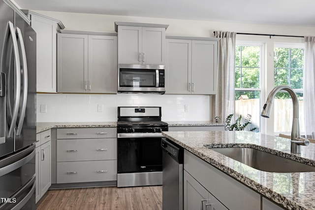 kitchen with a sink, appliances with stainless steel finishes, gray cabinets, and tasteful backsplash