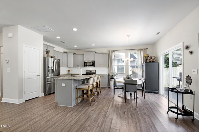 kitchen with wood finished floors, a breakfast bar, a sink, gray cabinetry, and stainless steel appliances