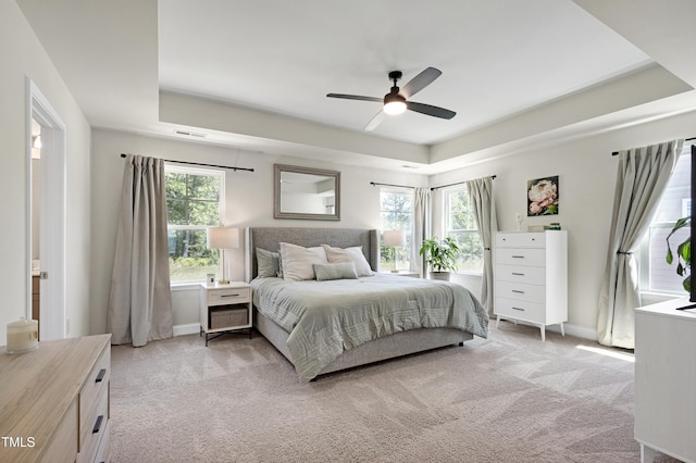 bedroom with light colored carpet, multiple windows, and a raised ceiling
