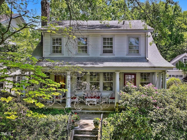 view of front of property with roof with shingles, a chimney, and a porch