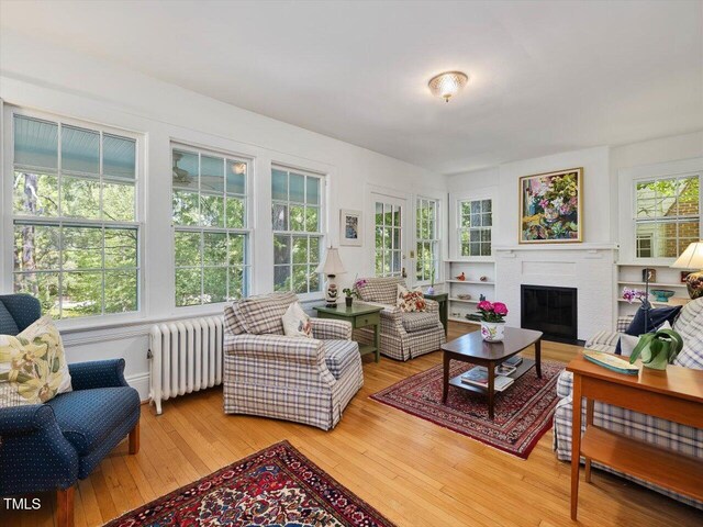 living area featuring light wood-style floors, radiator, and a brick fireplace