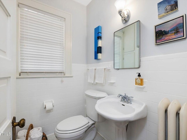 half bathroom featuring a sink, tile walls, a wainscoted wall, and toilet