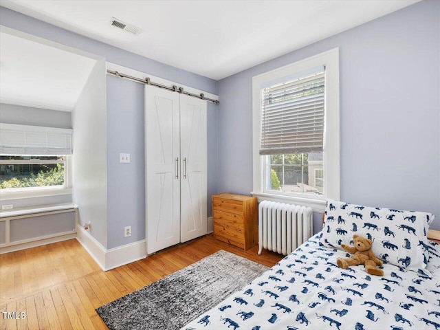 bedroom with visible vents, a barn door, baseboards, radiator, and hardwood / wood-style floors
