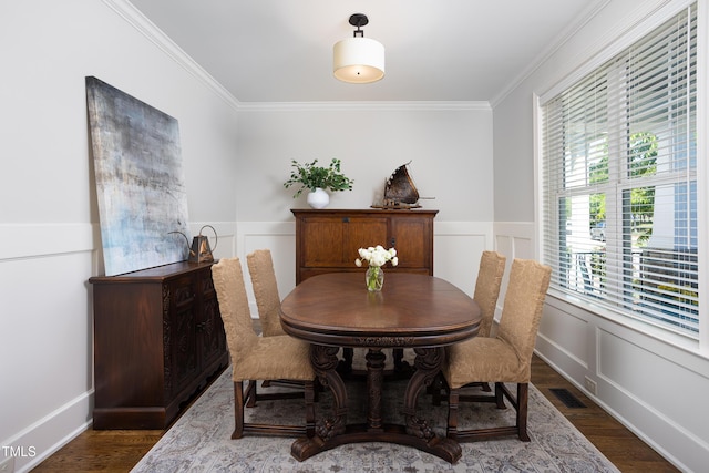 dining area featuring crown molding, a decorative wall, wood finished floors, and visible vents