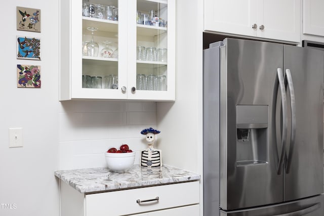 kitchen with decorative backsplash, glass insert cabinets, white cabinets, stainless steel fridge with ice dispenser, and light stone counters