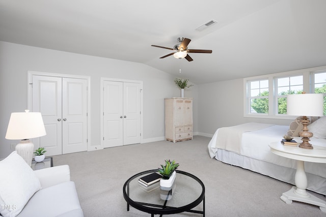 bedroom featuring carpet, two closets, baseboards, lofted ceiling, and visible vents