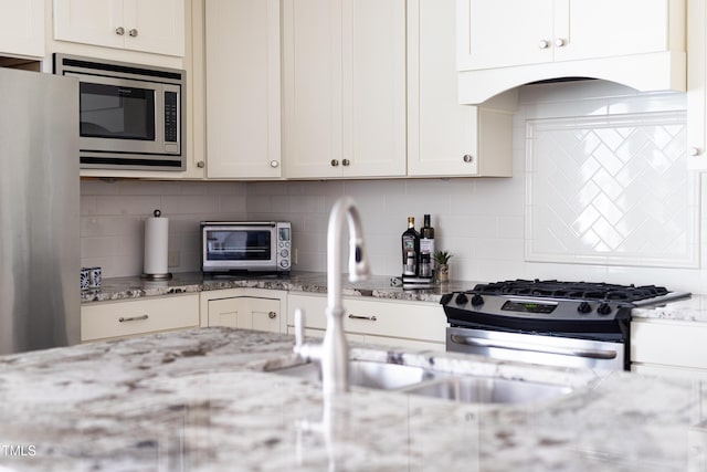 kitchen featuring backsplash, light stone countertops, a toaster, white cabinets, and stainless steel appliances