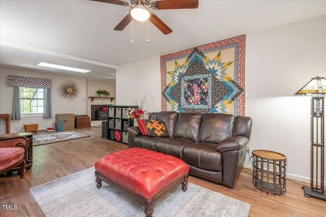 living area with ceiling fan, a textured ceiling, a brick fireplace, and wood finished floors