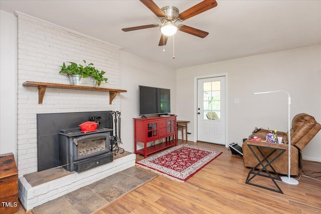 living room with a wood stove, wood finished floors, and ceiling fan