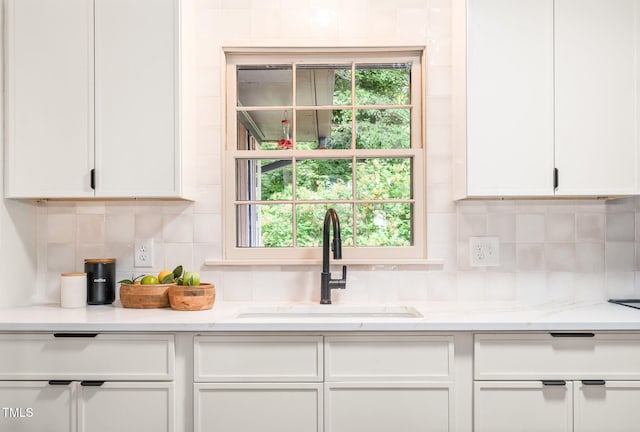 kitchen with backsplash, white cabinetry, light stone counters, and a sink