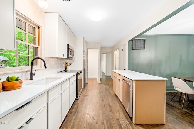 kitchen with stainless steel appliances, white cabinetry, a sink, and light wood-type flooring
