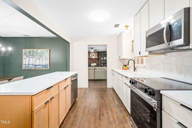 kitchen with backsplash, visible vents, wood finished floors, a sink, and stainless steel appliances