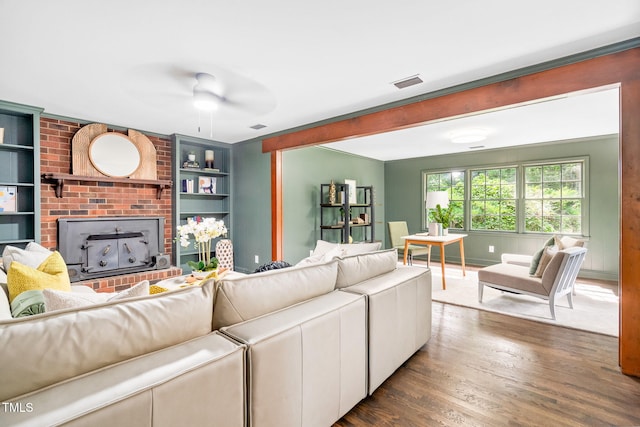 living area with visible vents, a fireplace, built in shelves, a ceiling fan, and dark wood finished floors