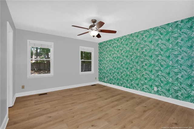 spare room with a ceiling fan, visible vents, wood finished floors, baseboards, and an accent wall