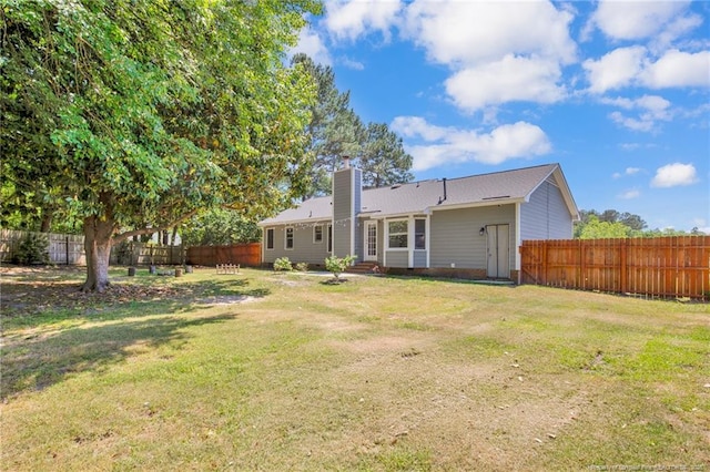 back of house with a fenced backyard, a chimney, and a yard