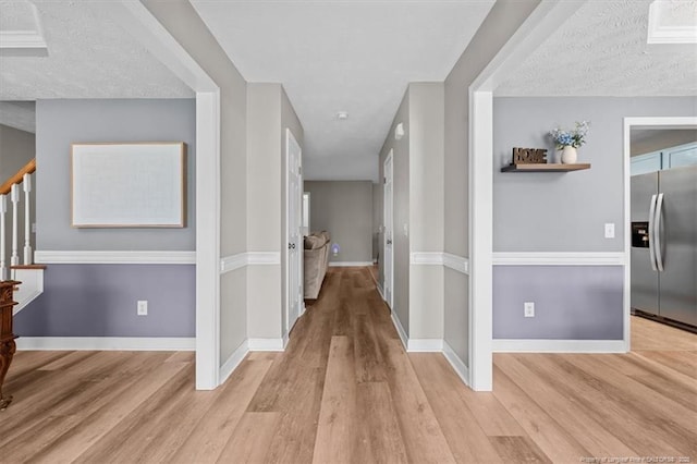 hallway featuring light wood-style floors, a textured ceiling, stairs, and baseboards