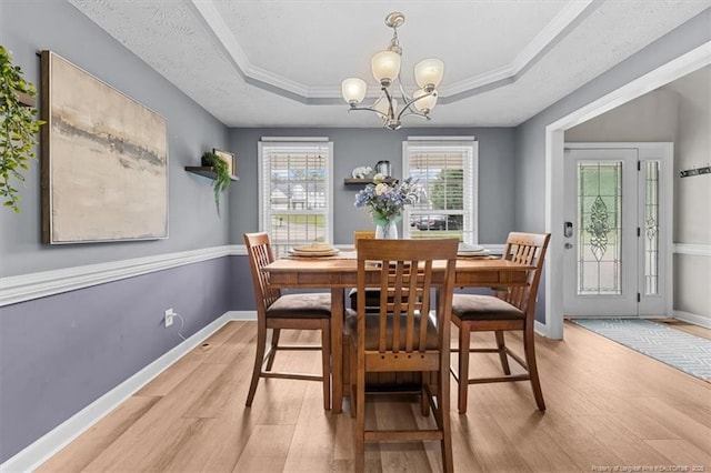 dining space with crown molding, baseboards, an inviting chandelier, a tray ceiling, and light wood-style flooring