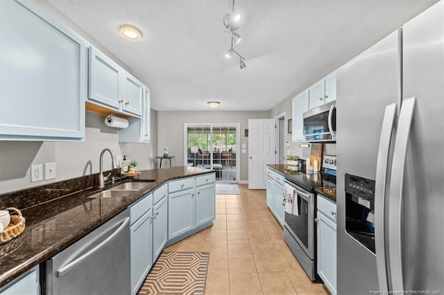 kitchen featuring a sink, dark stone countertops, appliances with stainless steel finishes, light tile patterned floors, and blue cabinetry