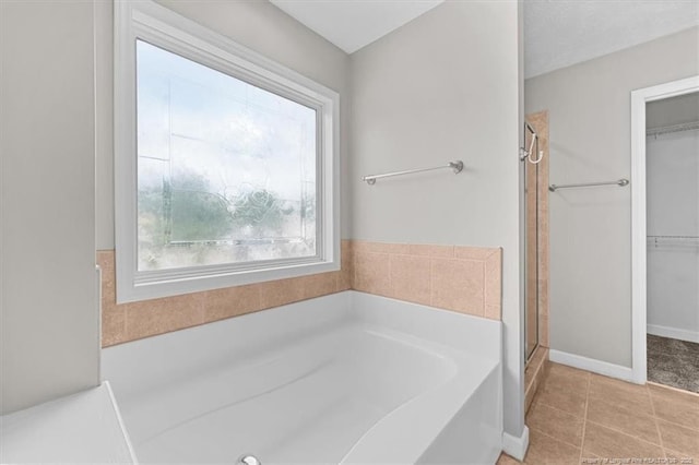 full bath with tile patterned flooring, baseboards, a walk in closet, a bath, and a shower stall